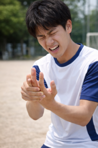 突き指で指の痛みに顔をしかめながら手を押さえる日本人男性（屋外・スポーツ中）