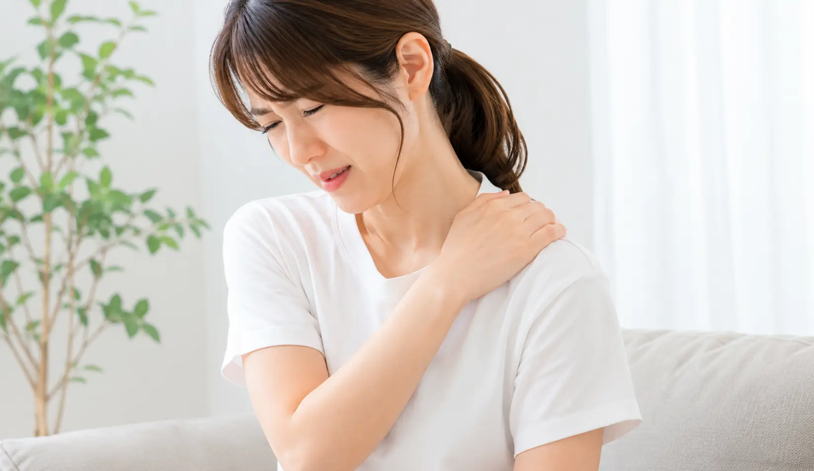 肩に痛みを感じ、肩まわりを手で押さえている女性のイメージ