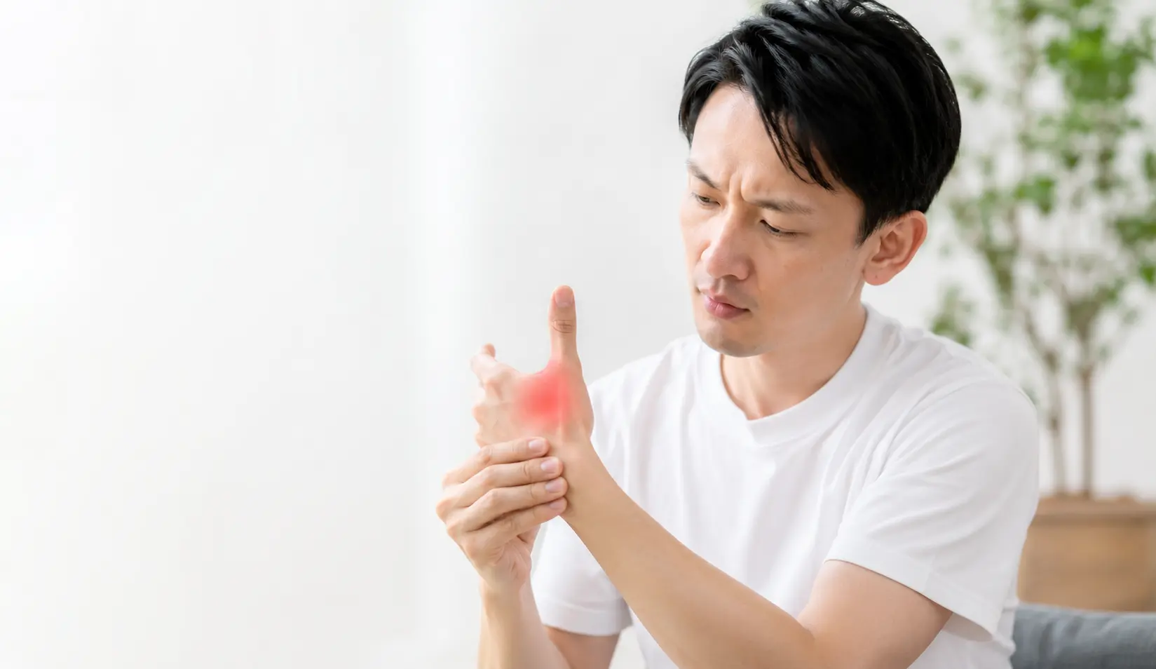 親指の付け根の関節に痛みを感じ、手を押さえる男性
