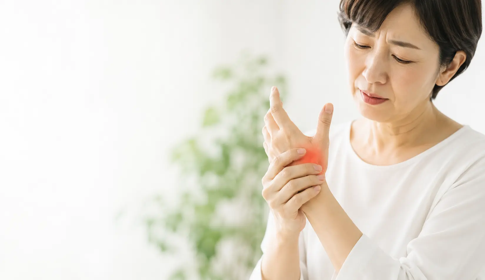 親指の付け根に痛みを感じ、手を押さえる女性