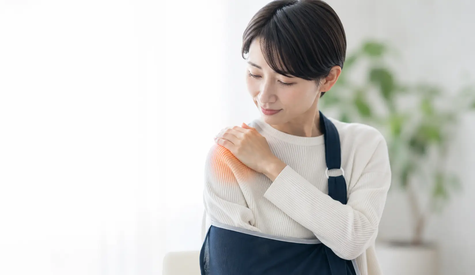 上腕骨近位部骨折後の肩に痛みを感じ、腕を固定しながら肩を押さえる女性