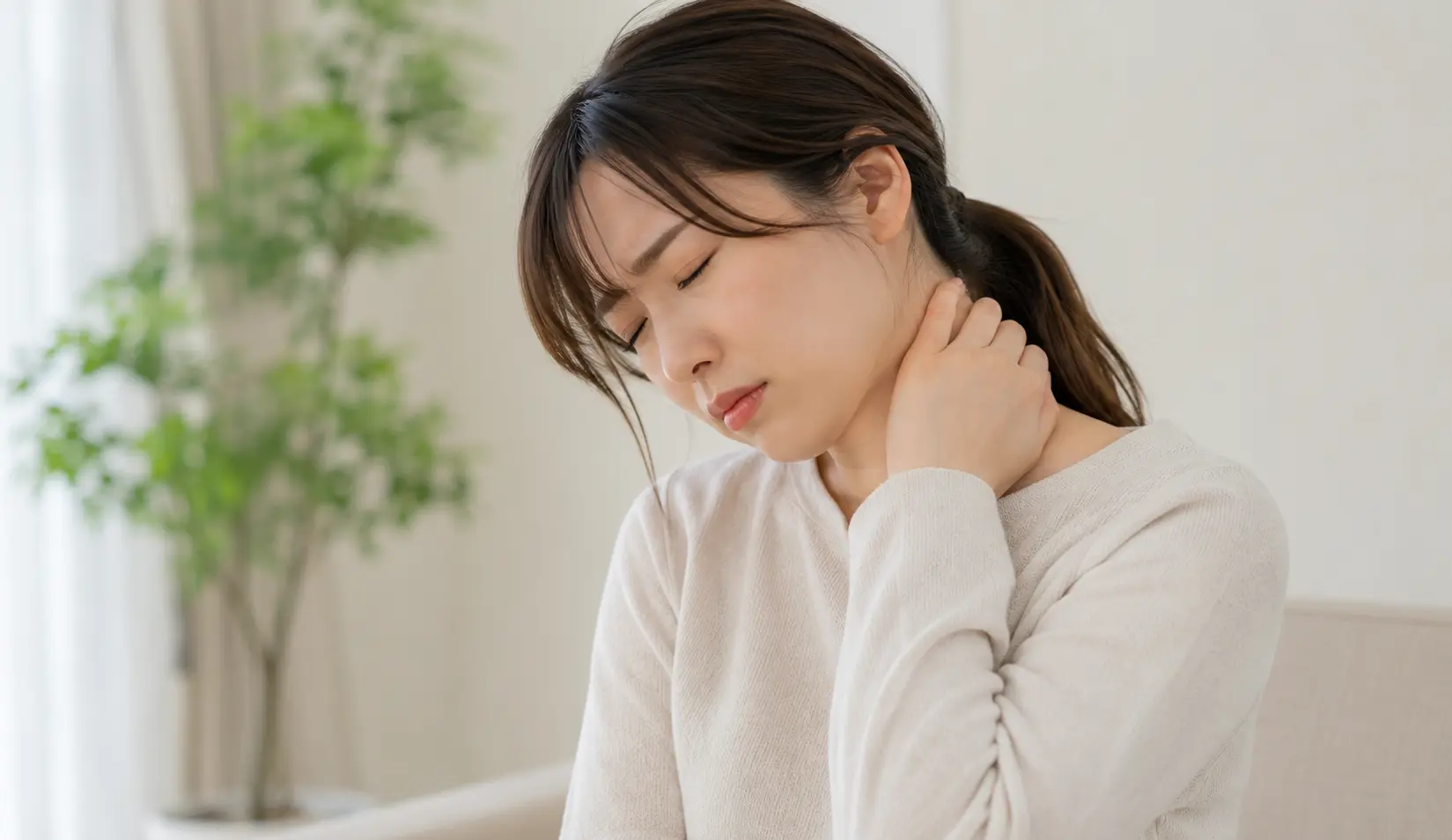首の痛みを感じ、つらそうに首の後ろを押さえる女性|多摩鍼灸整骨院 高幡不動院