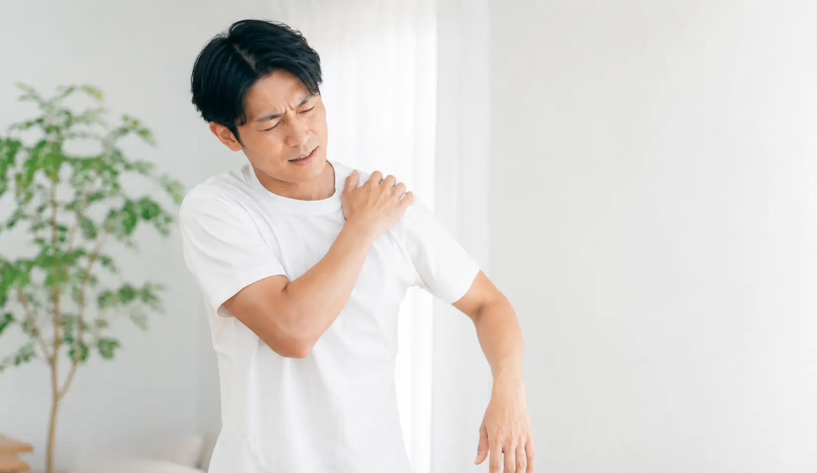 肩関節脱臼による強い痛みを感じ、肩を押さえる男性