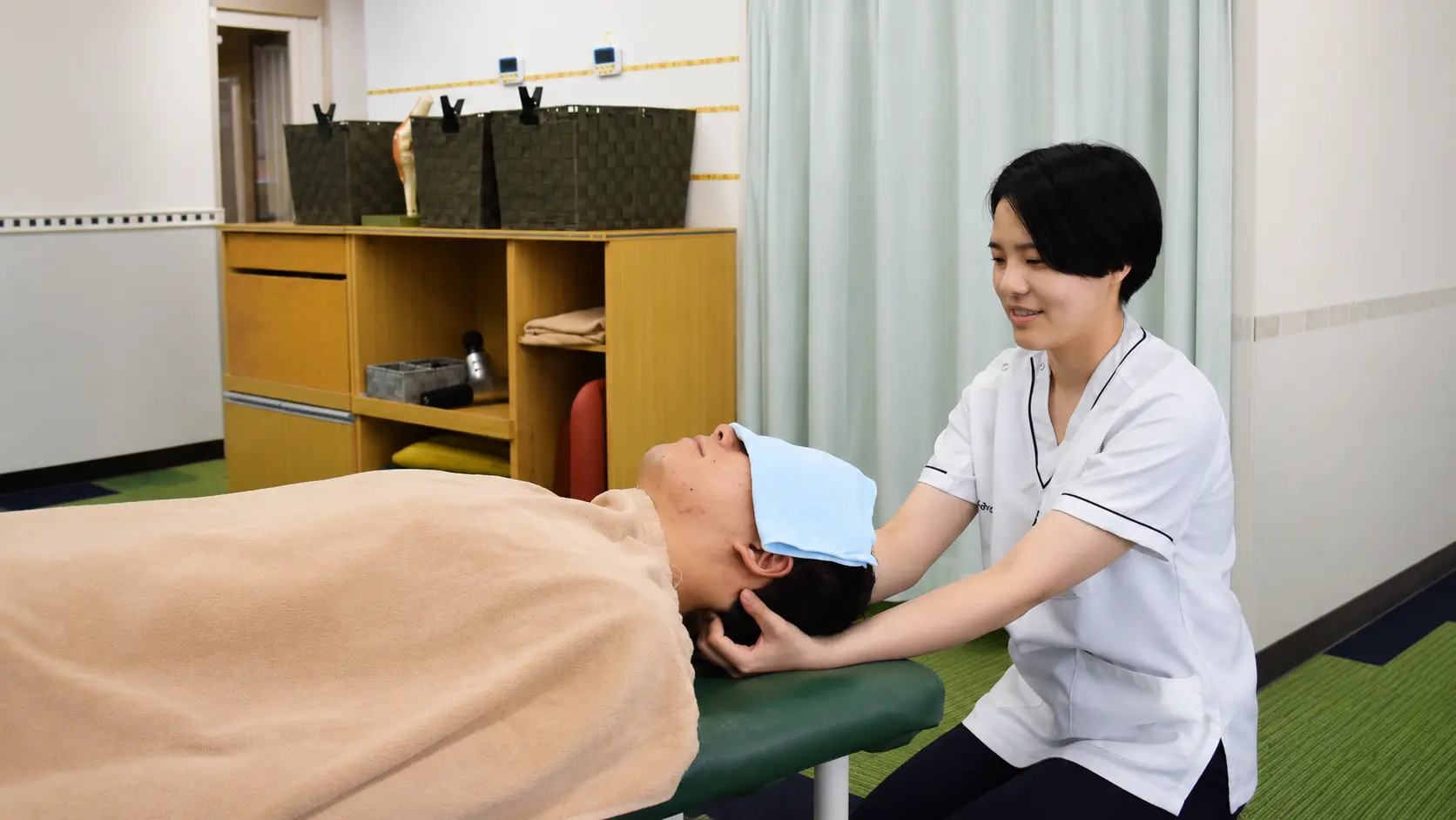 多摩鍼灸整骨院 高幡不動院で、スタッフが患者さまの首まわりを丁寧に施術している様子。首・肩の痛みや頭痛、身体の不調など、一人ひとりの状態に合わせて施術を行っています。
