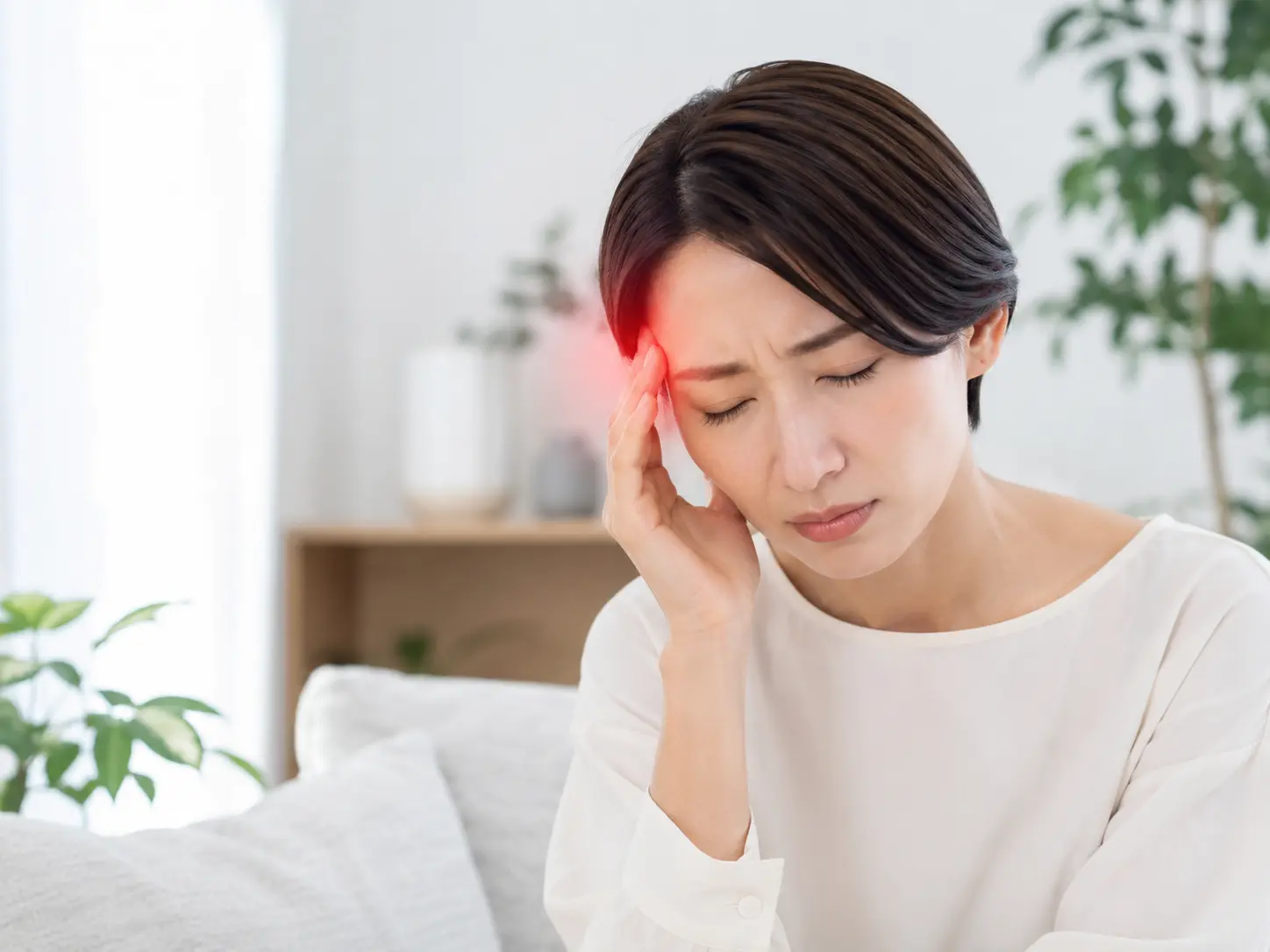 頭痛を感じ、こめかみを手で押さえてつらそうにしている女性の様子