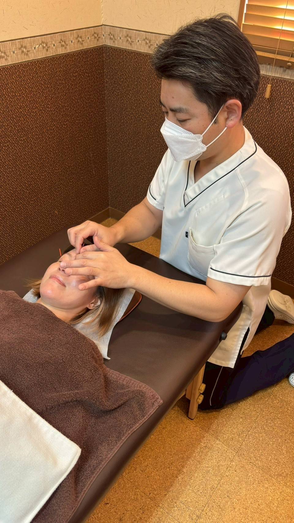 高倉本院の矢崎院長が、花粉症に悩む患者様の顔まわりに丁寧に鍼施術を行っている様子。落ち着いた個室空間で安心して受けられる施術風景。
