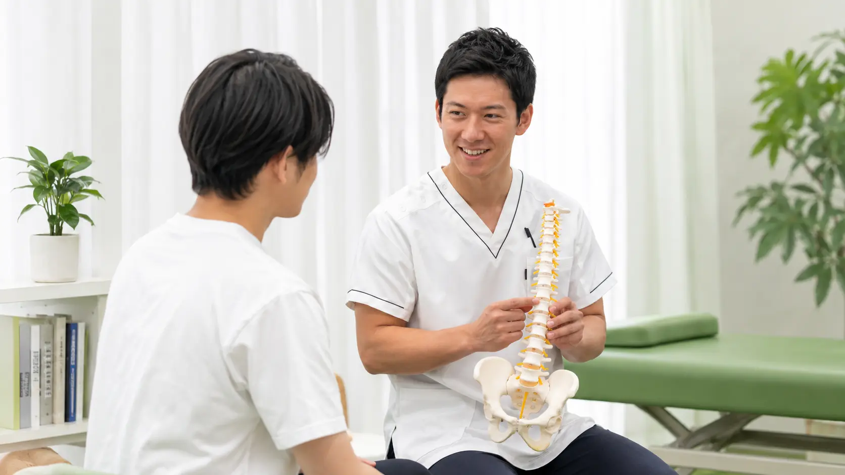 急な腰痛やぎっくり腰の方に対して、施術者が背骨の模型を使いながら腰の状態を丁寧に説明している検査・相談イメージ